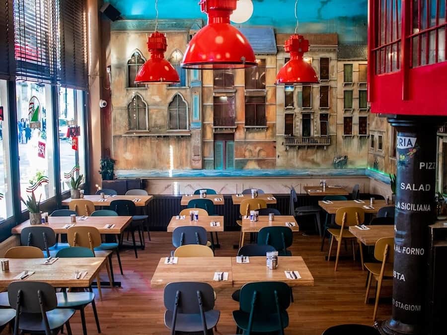 Un restaurante con mesas y sillas de madera, luces colgantes rojas y un mural en la pared.