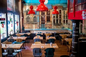 A restaurant with wooden tables and chairs, red pendant lights, and a mural on the wall. - Hotel Doria (Amsterdam)