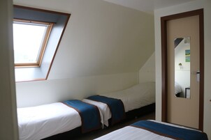 Quarto com duas camas individuais, um claraboia, uma porta com espelho e uma janela pequena.
