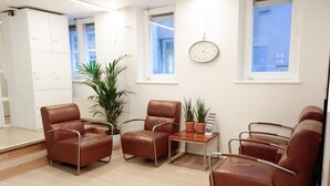 A modern room with leather chairs, a small table, potted plants, and a clock on the wall. - Hotel Doria (Amsterdam)