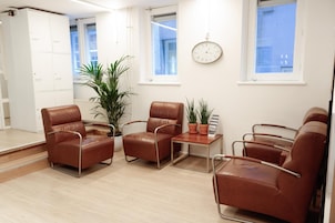 Ein modernes Zimmer mit Ledersesseln, einem kleinen Tisch, Topfpflanzen und einer Wanduhr.