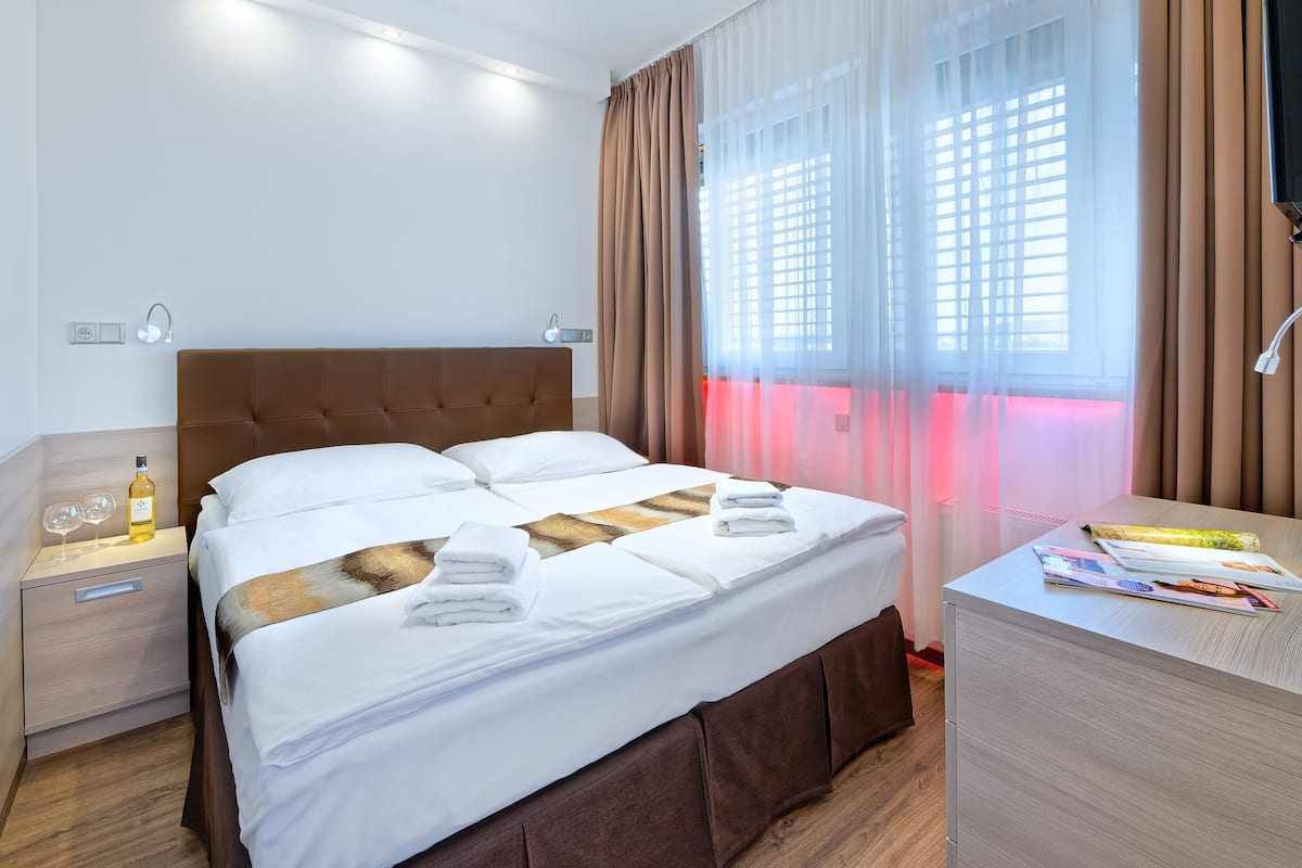 A hotel room with a large bed, bedside tables, a desk, and a window with curtains.