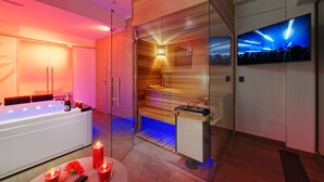Et moderne spa-rum med et stort badekar, en sauna og et tv, der viser en koncert.