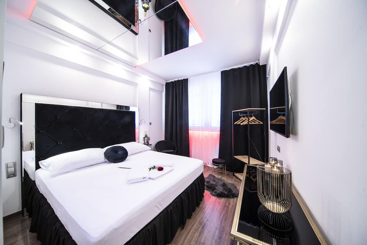 A modern hotel room with a large bed, a vanity, a mirror, and a wardrobe with hanging clothes.
