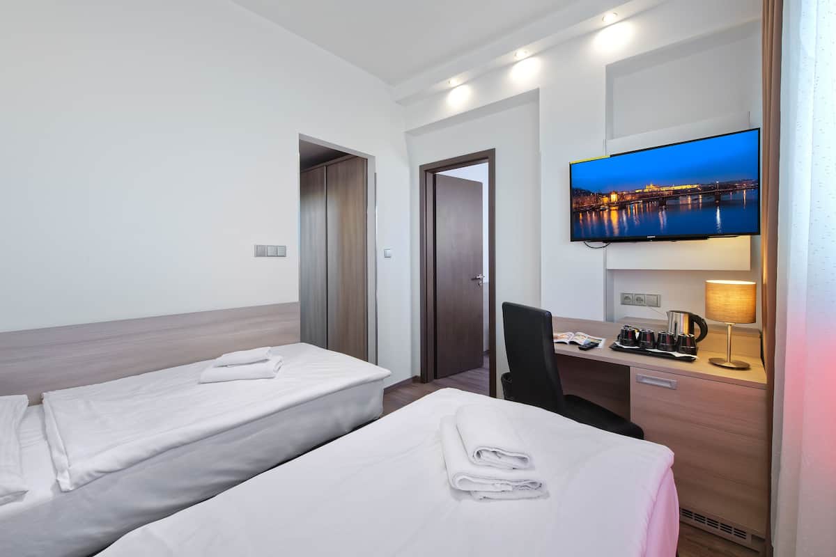 A hotel room with two single beds, a desk with a lamp, a television, and a view of a cityscape.