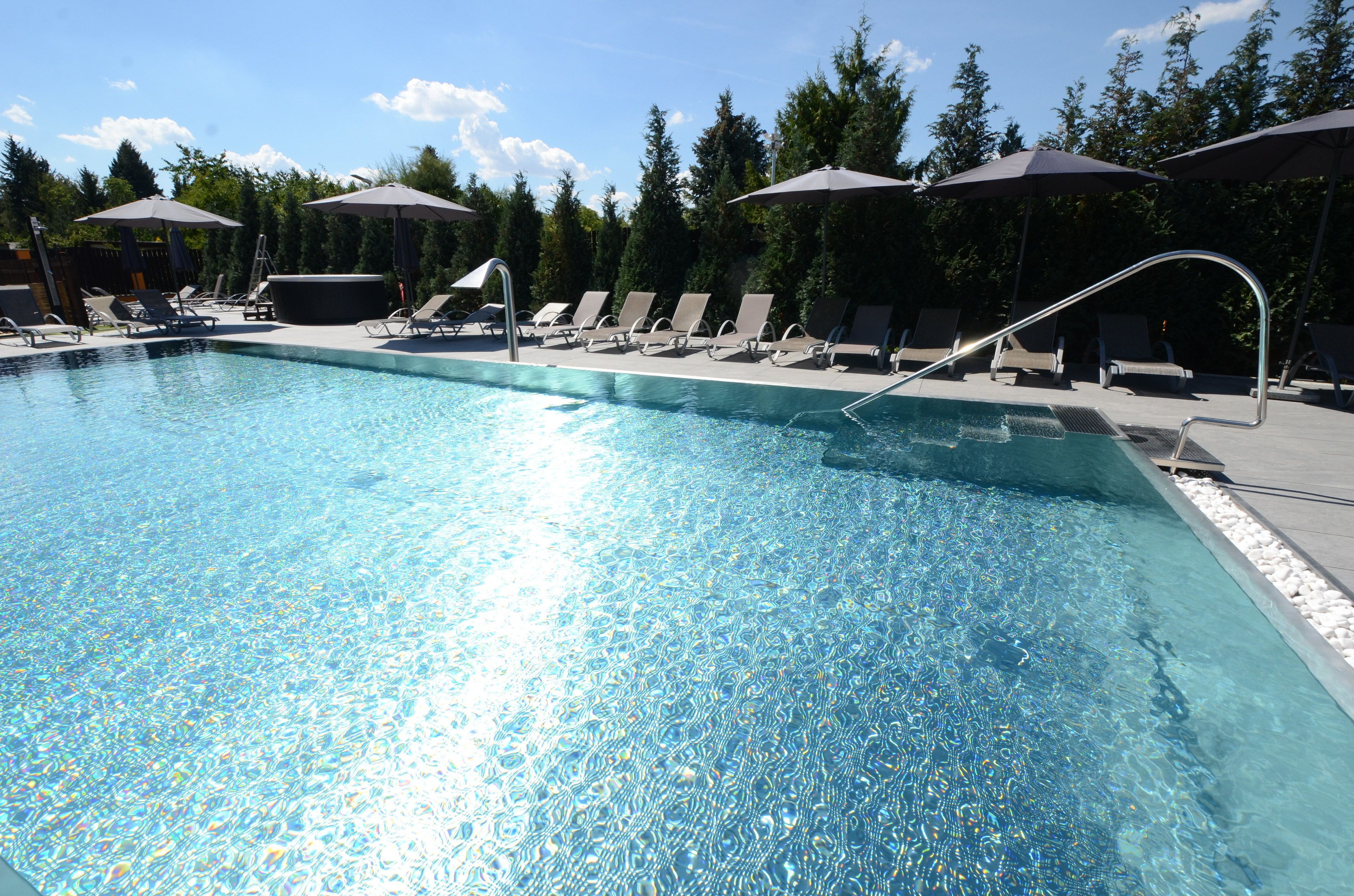 Ein klares Schwimmbecken mit Liegestühlen und Sonnenschirmen, umgeben von Bäumen.