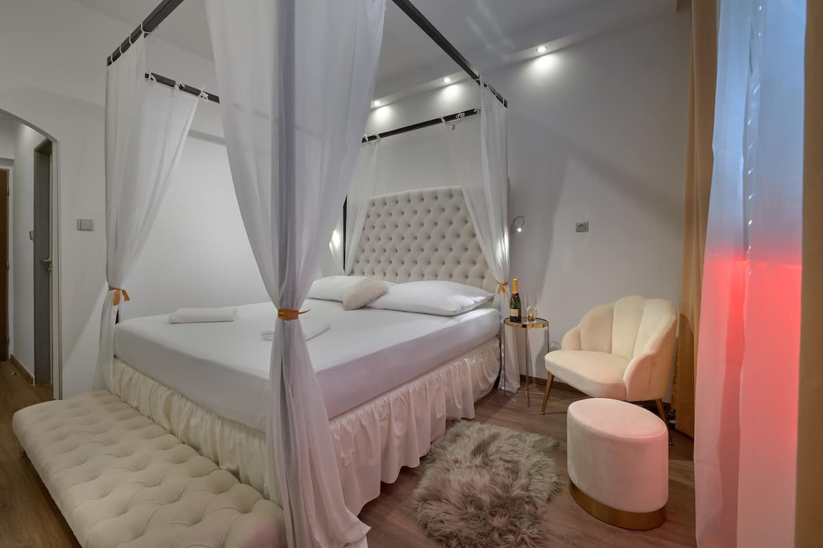 A bedroom with a canopy bed, a tufted headboard, a bench, a fluffy rug, and a side table with a bottle.