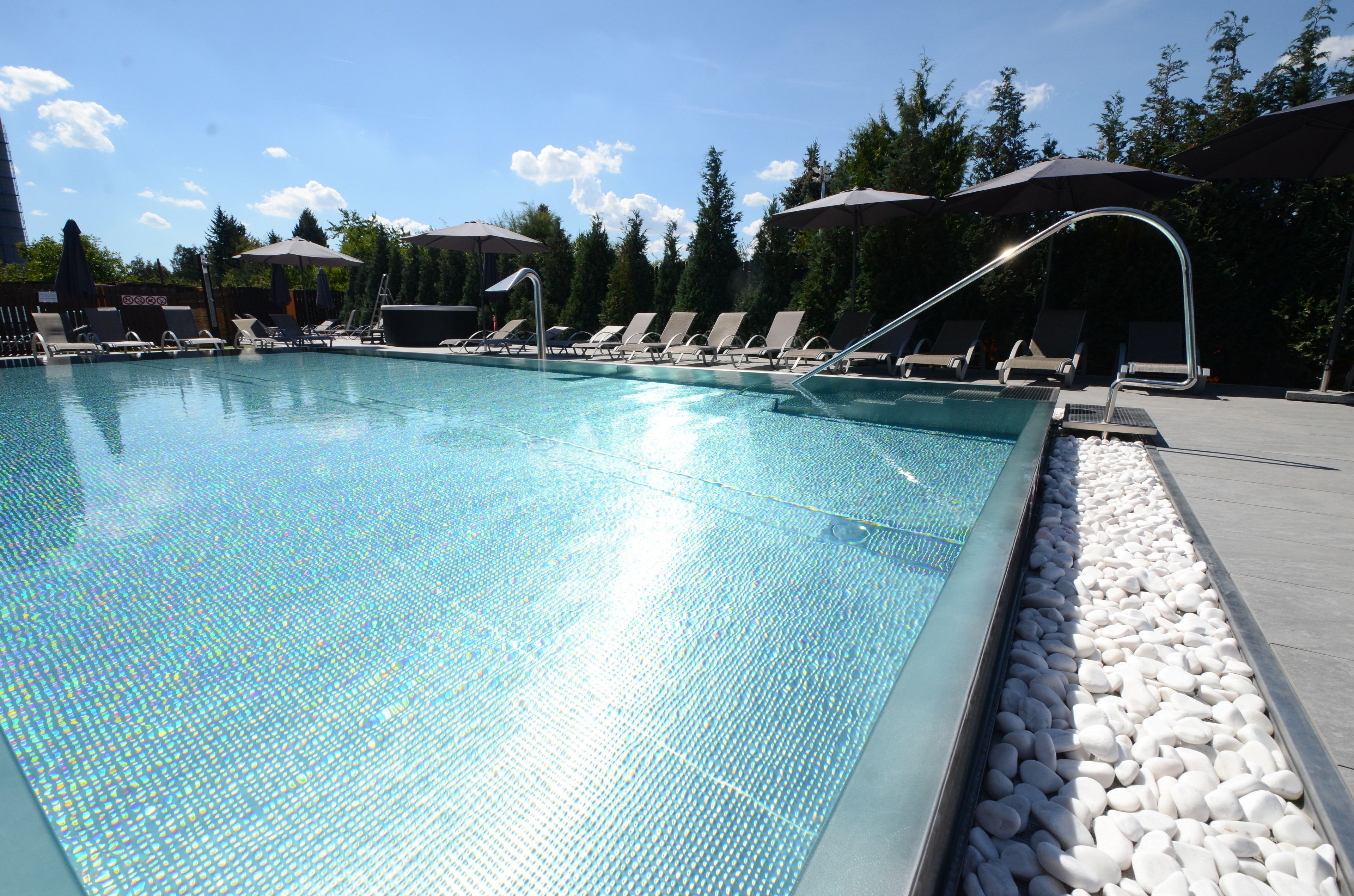 A swimming pool with lounge chairs and umbrellas, surrounded by trees.