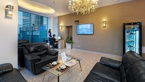Et hotellobby med lædersofaer, et glaskaffebord med en menu, en receptionsdisk, en digital skærm og et køleskab.
