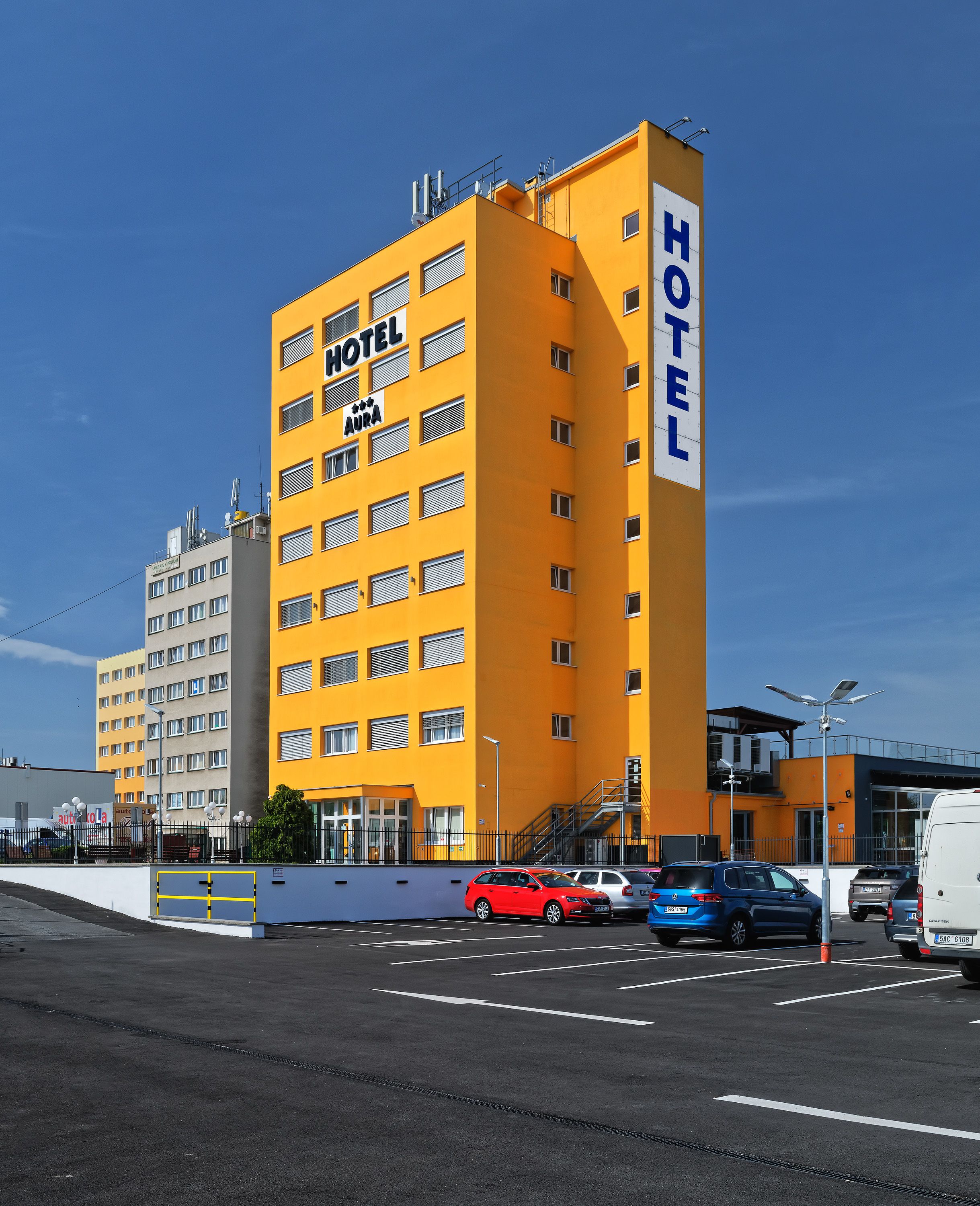 A yellow multi-story hotel with a sign reading "HOTEL AURA" and "HOTEL".
