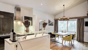 Una cuina moderna amb una illa central, zona de menjador amb cadires i una finestra gran amb cortines.