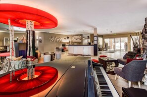 Un salon moderne avec un piano, une structure circulaire rouge et un coin cuisine à l’arrière-plan.