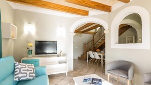 Una sala de estar moderna con un televisor de pantalla plana, un sofá con cojines estampados, una mesa de centro y una escalera que conduce a un comedor.