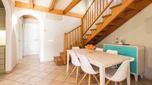 Un comedor con escalera de madera, sillas blancas y un mueble turquesa.