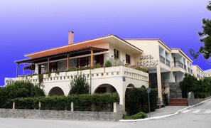 A two-story hotel with a covered patio and a stone facade. - Ifestos Hotel (MIRINA)