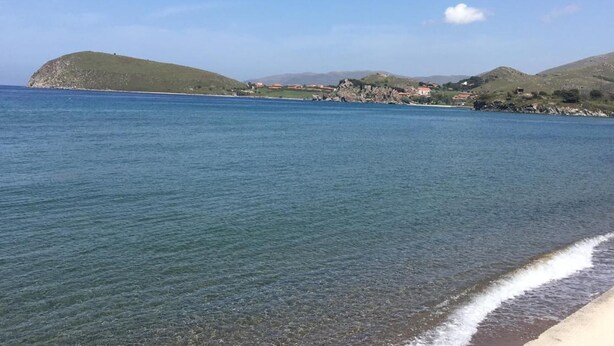 Un paisaje costero con aguas azules cristalinas, una playa arenosa y colinas al fondo.