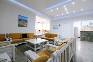 A modern hotel lobby with a seating area, a reception desk, and a view of the dining area. - Ifestos Hotel (MIRINA)