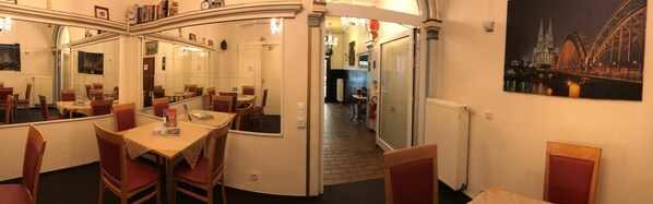 Un restaurante con una pared curva, varias mesas y sillas. Hay una pintura de un puente en la pared.