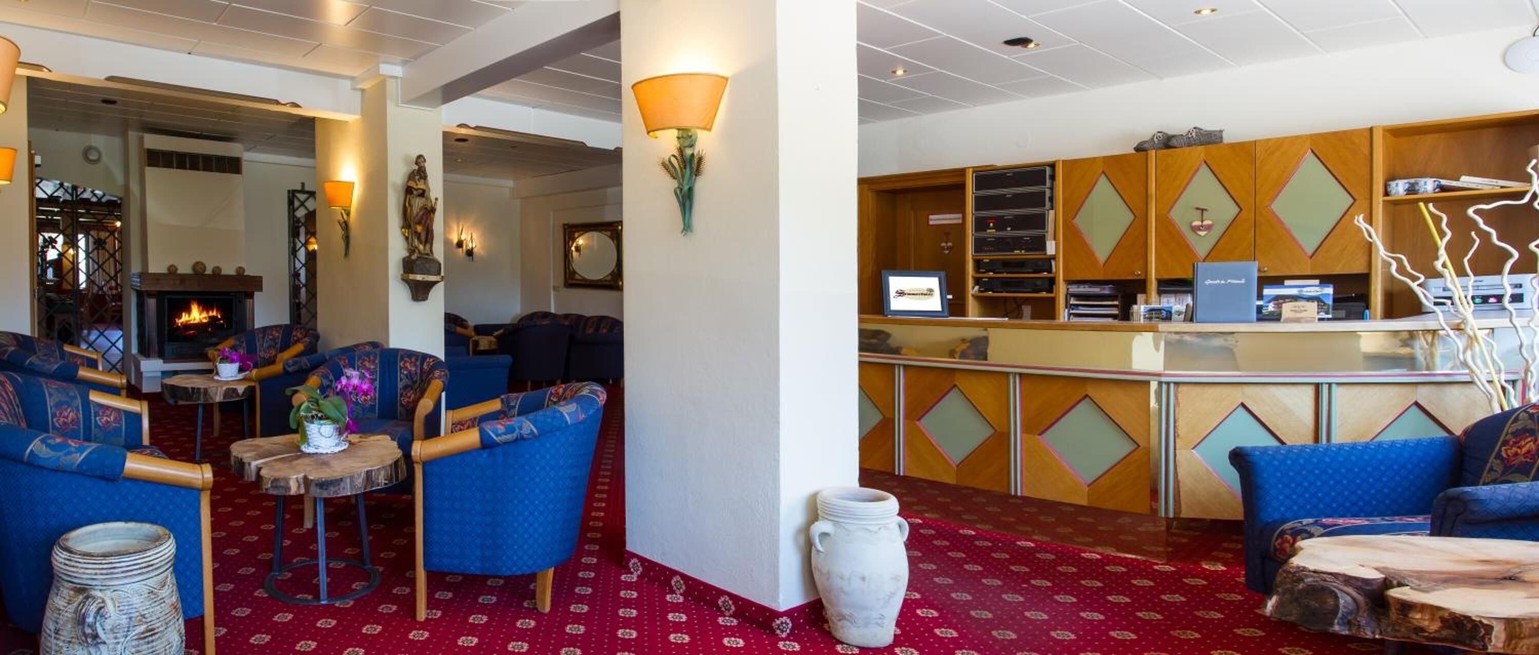 Un hall d’hôtel doté de sièges recouverts d’un tissu bleu, d’une cheminée et d’un comptoir d’accueil avec un revêtement mural en bois.