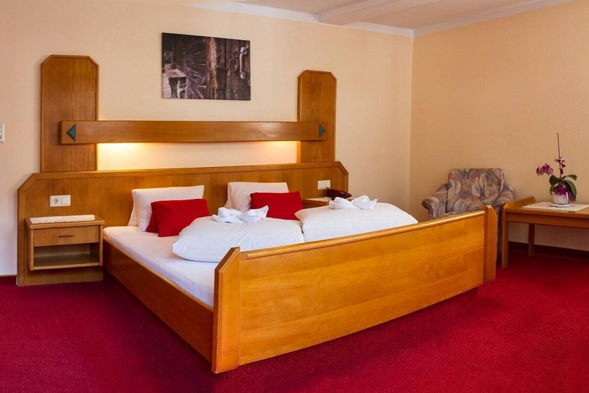 A hotel room with a wooden bed, a TV, a desk with a chair, and a red carpet.