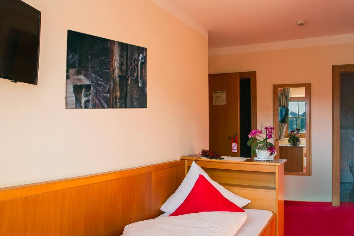 A hotel room with a bed, a desk, a telephone, and a painting on the wall.