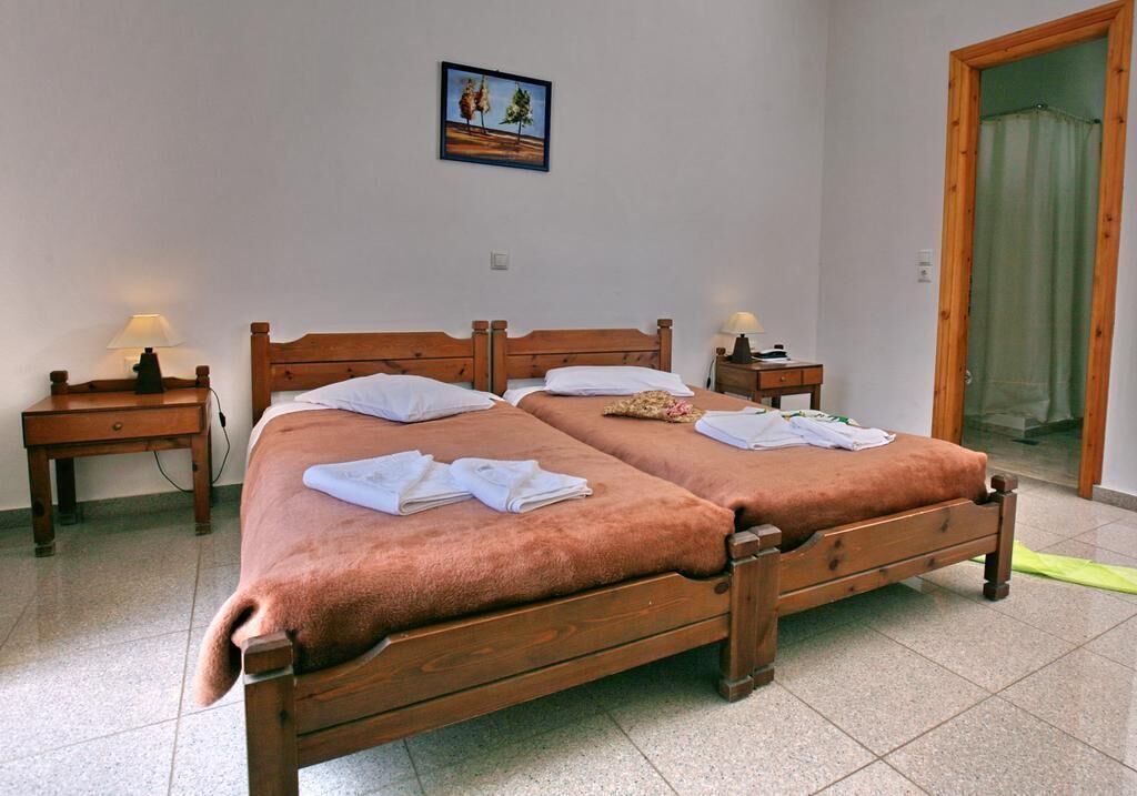 A double bed with two nightstands, each with a lamp, in a room with a tiled floor and a door with a green curtain.