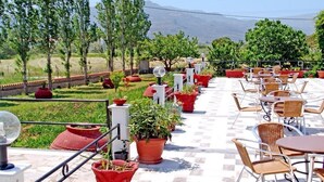An outdoor patio with tables and chairs, surrounded by potted plants and a view of distant mountains. - Pela Hotel (Lesvos)