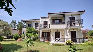 A two-story building with balconies, a garden with potted plants, and a clear sky. - Pela Hotel (Lesvos)