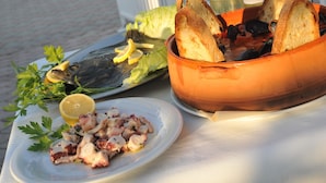 A table with a plate of octopus salad, a bowl of bread, and two bottles of wine on a terrace overlooking the sea. - Villaggio Capo Vieste Camping (Vieste)