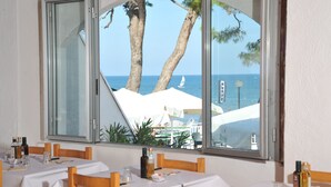 A dining area with tables set for two, overlooking a beach with palm trees and a sailboat. - Villaggio Capo Vieste Camping (Vieste)