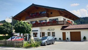 A two-story building with a balcony, a sign reading "Alpenland," and a car parked in front. - Alpenland (FLACHAU)