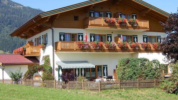 A two-story building with wooden balconies, a covered outdoor seating area, and a mountain backdrop. - Alpenland (FLACHAU)