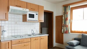 A compact kitchen with wooden cabinets, a microwave, a sink, and a window with curtains. - Alpenland (FLACHAU)