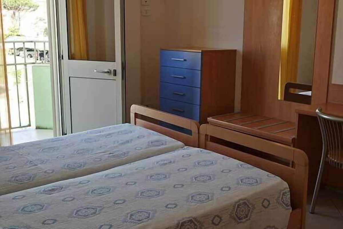Una habitación con dos camas, un escritorio de madera y un archivador azul.