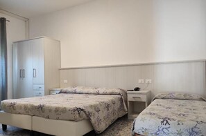 A bedroom with two beds, a wardrobe, a bedside table with a lamp, and a wall-mounted power outlet. - Hotel Vianello (Jesolo)