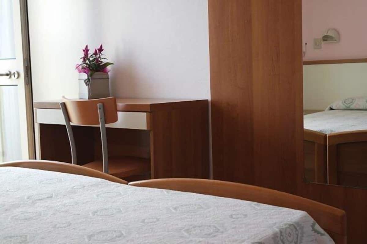 Una habitación de hotel con una cama, un escritorio de madera, una silla y una mesita con un jarrón de flores.