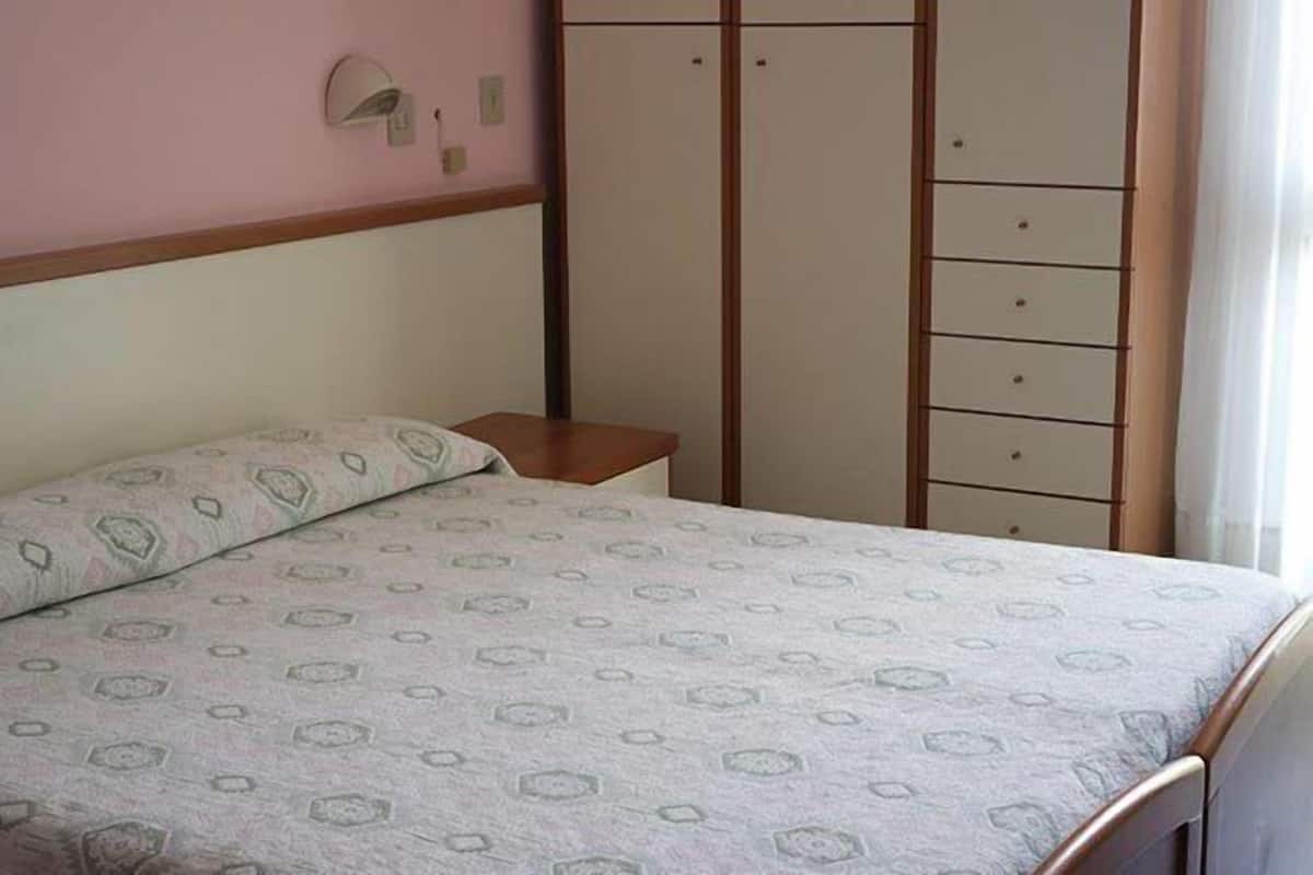 Un dormitorio con cama, mesita de noche, armario e iluminación en la pared.