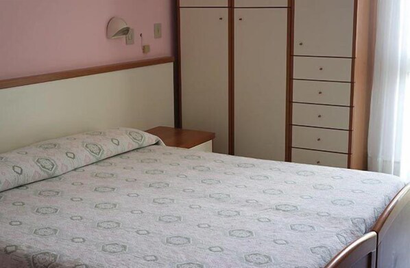 A bedroom with a bed, a nightstand, a wardrobe, and a wall-mounted light fixture. - Hotel Vianello (Jesolo)