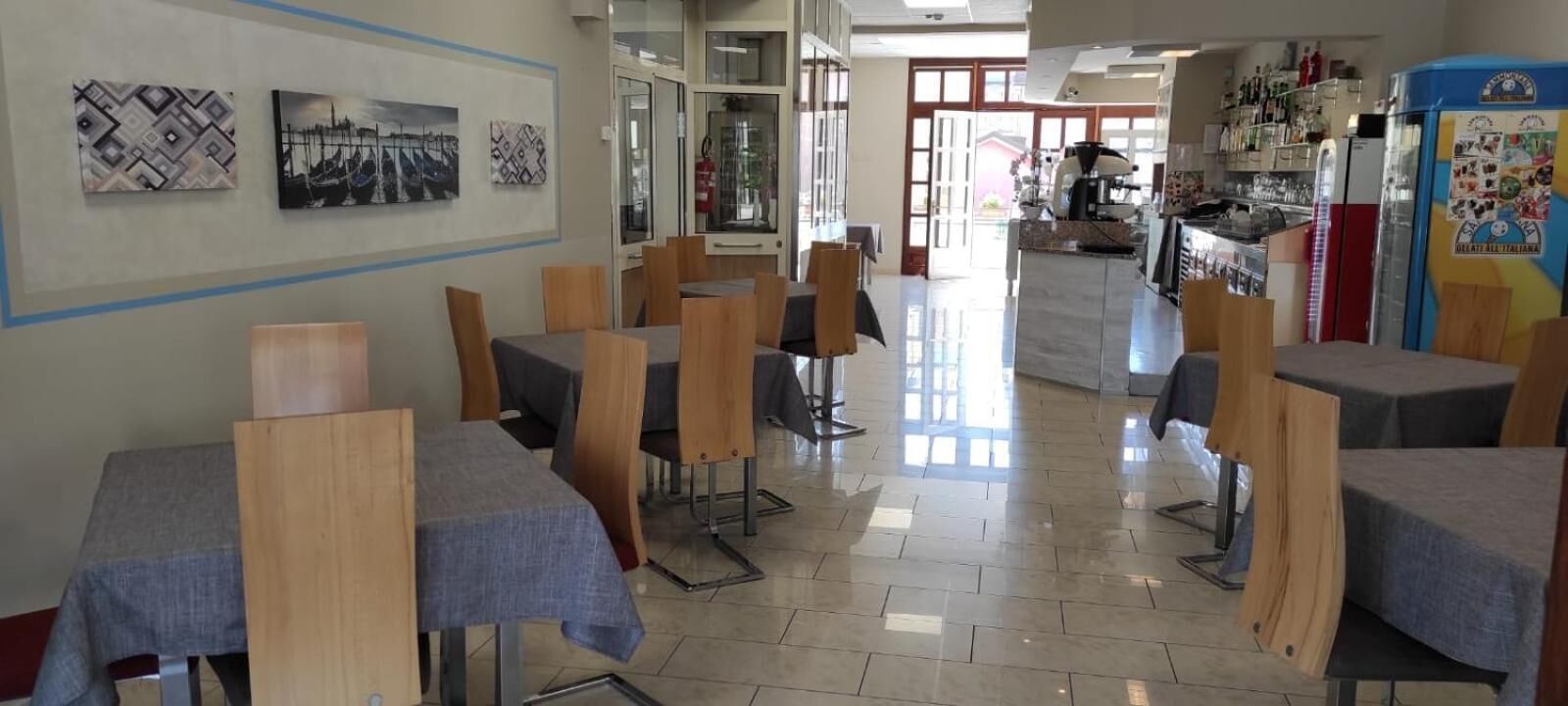Zona pranzo con tavoli e sedie, cucina sullo sfondo e opere d'arte alle pareti.