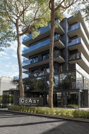 Een modern hotelgebouw met meerdere balkons, een bord met de tekst 'CoAst Hotel & Spa' en een verzorgd buitengebied met bomen en struiken.
