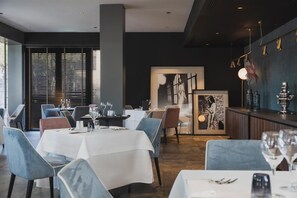 Een modern restaurantinterieur met gedekte tafels, een bar met decoratieve elementen en kunstwerken in lijsten aan de muren.