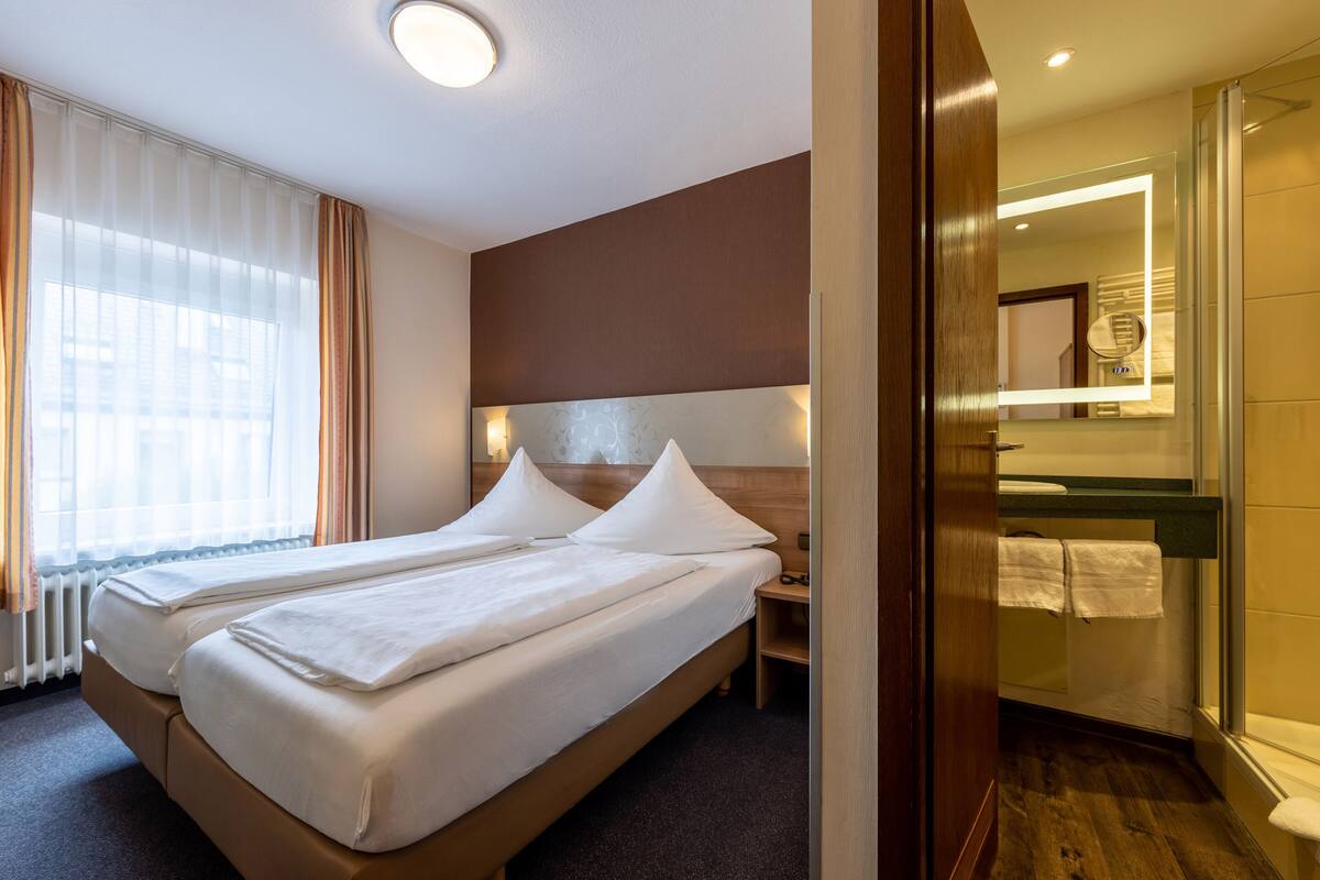 Habitación de hotel con dos camas, un espejo grande, cabecera de madera y vistas a la ciudad a través de la ventana.