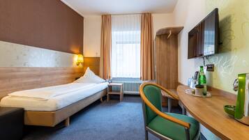 A hotel room with a bed, a desk with a chair, a television, and a window with curtains.