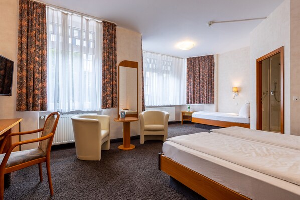 Habitación de hotel con cama, escritorio, silla, mesita, espejo y baño con ducha.
