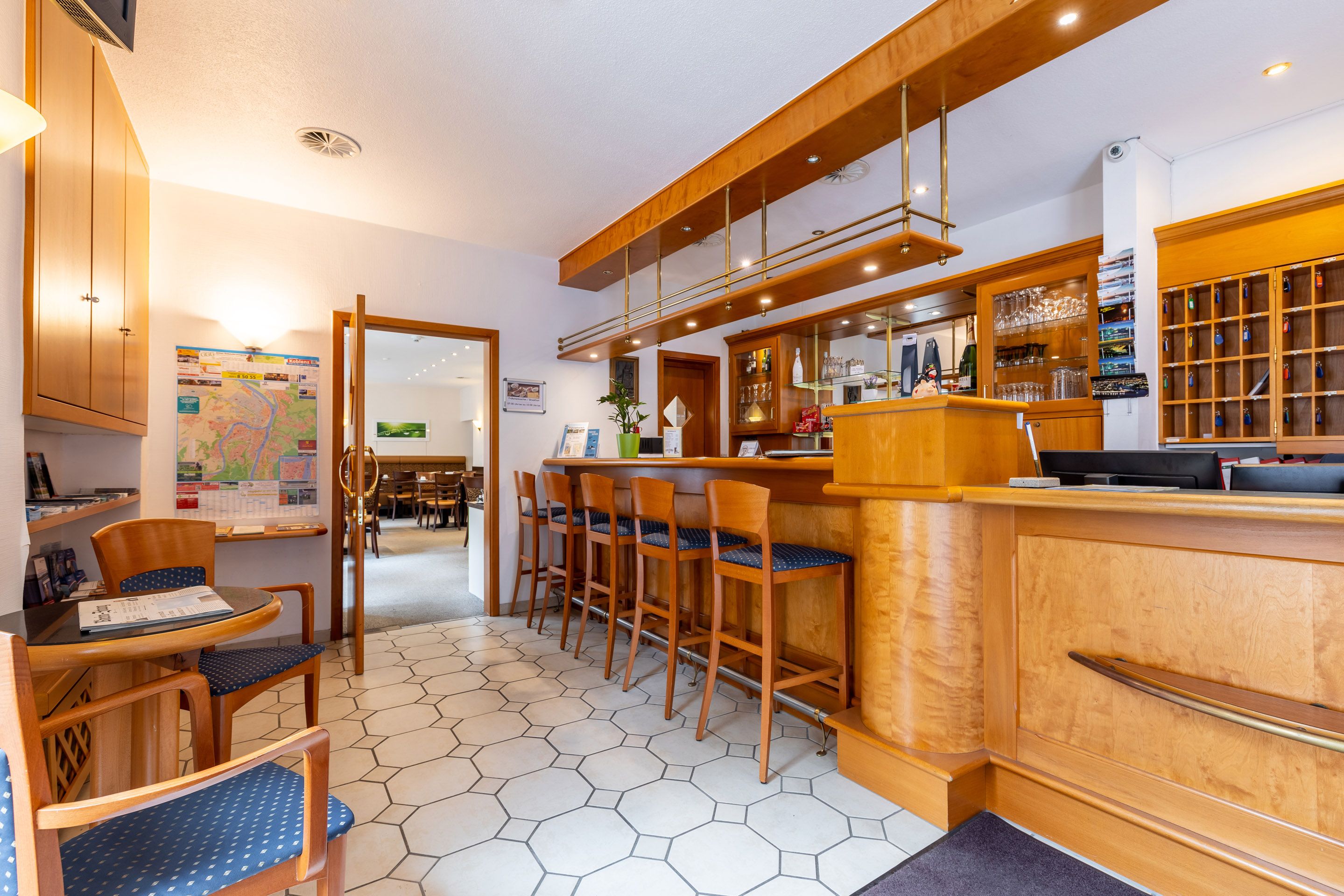 Vestíbulo de hotel con mostrador de recepción de madera, zona de bar y asientos con sillas acolchadas azules.