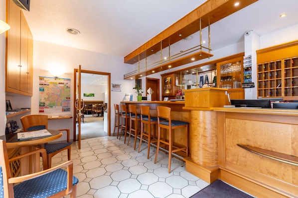 Eine Hotelhalle mit Holzbartresen, Barbereich und Sitzgelegenheiten mit blau gepolsterten Stühlen.