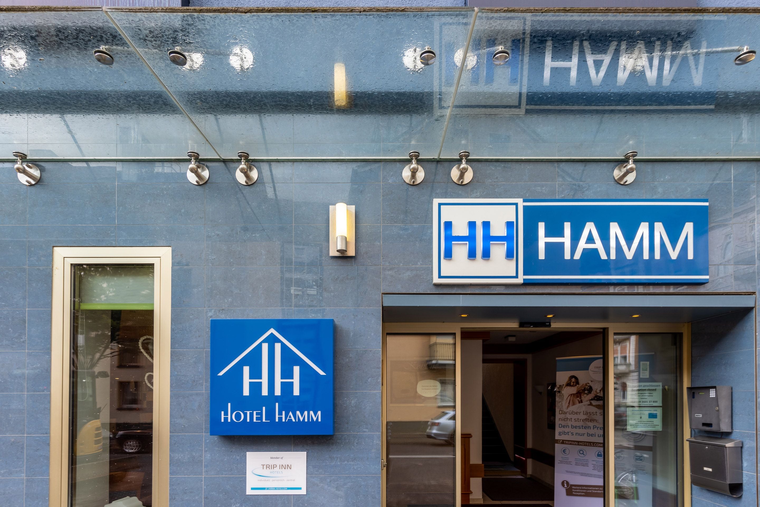 Entrada de un hotel con un cartel que dice "HOTEL HAMM" y un cartel más pequeño que indica "TRIP INN".