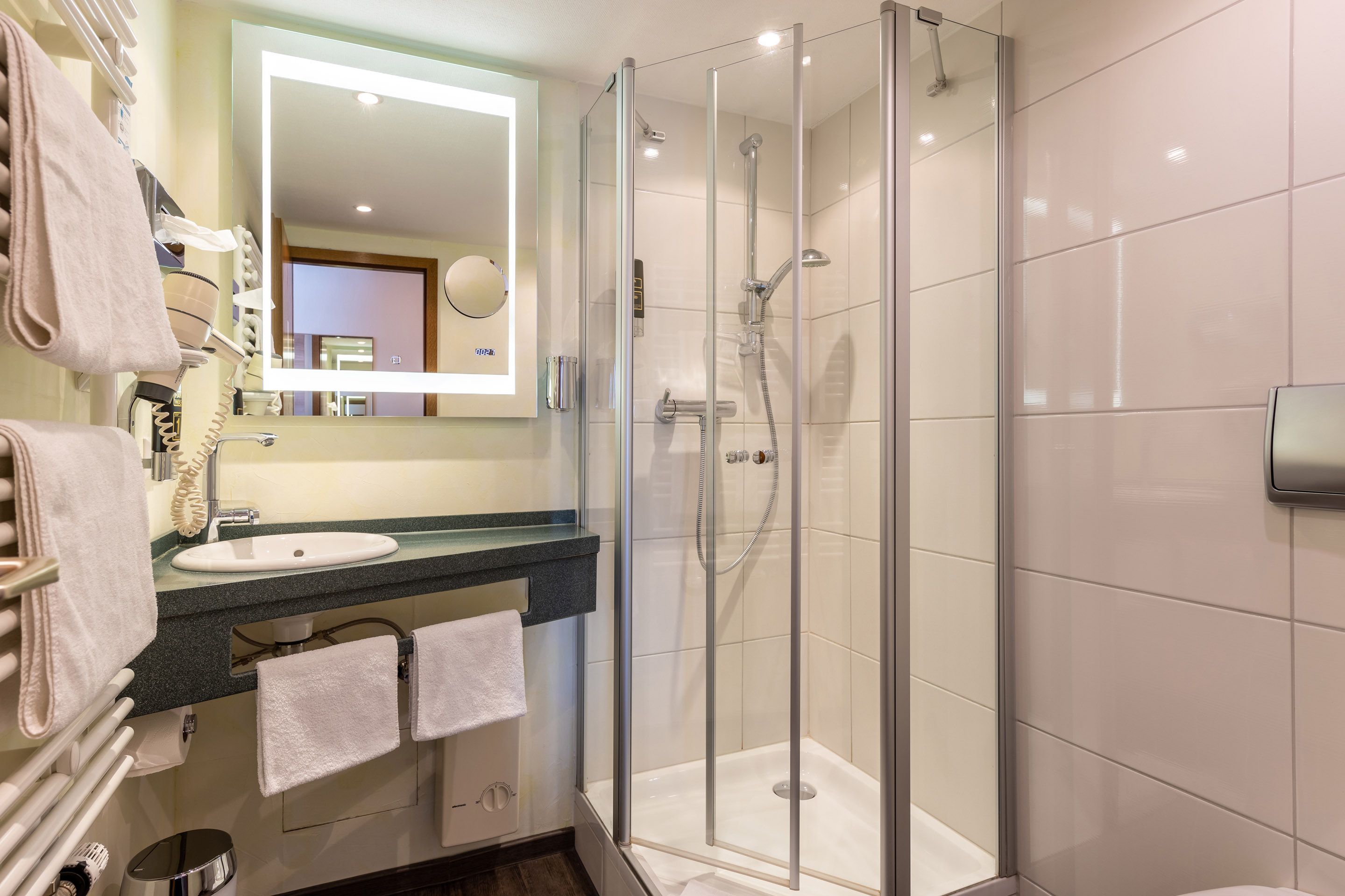 Ein modernes Badezimmer mit einer ein Glaswand umgebenen Dusche, einem Waschbecken mit Spiegel und Handtüchern auf einem Ablagekorb.