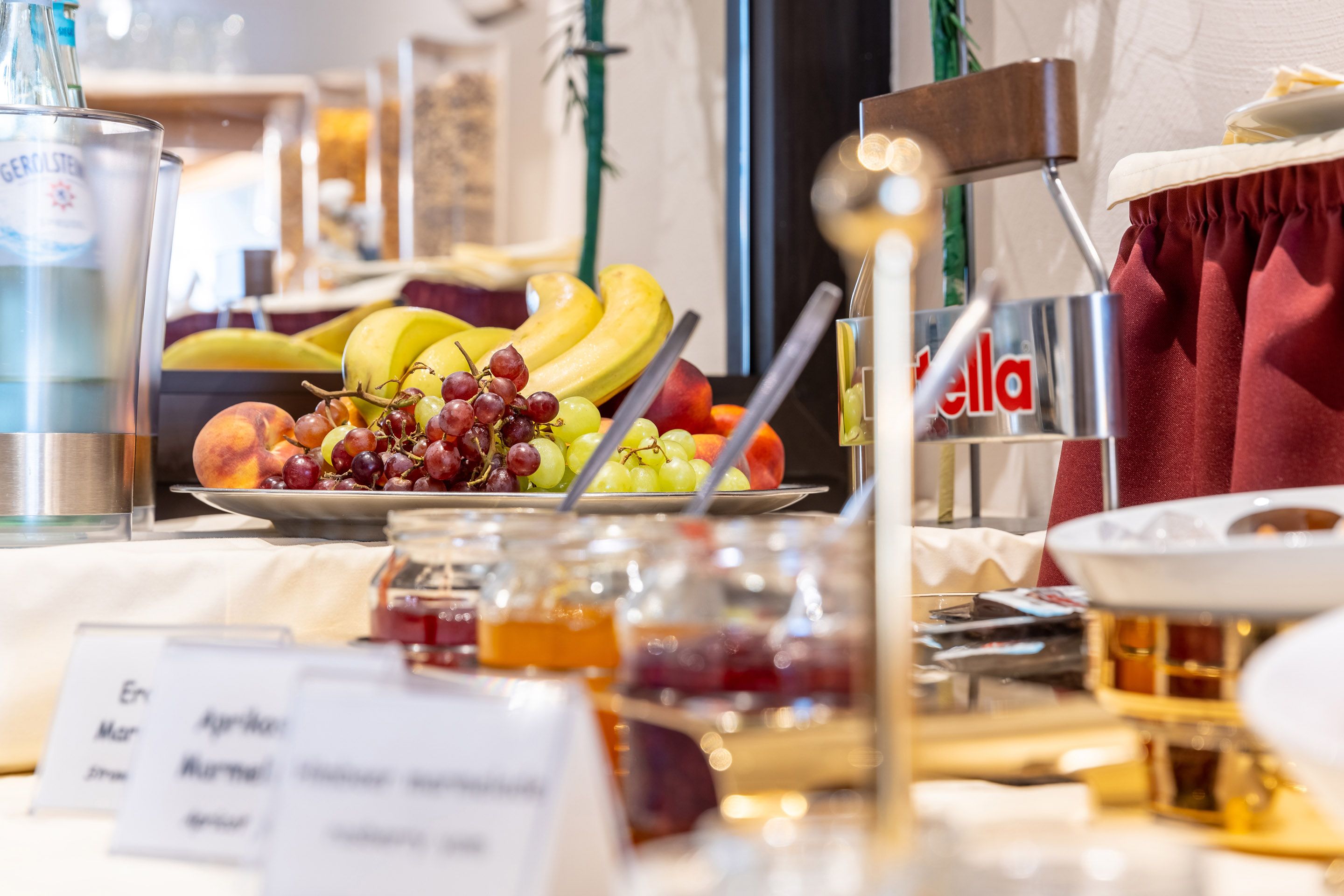 A buffet table with various fruits, a bottle of Gerolsteiner beer, and a sign with the word "ella".