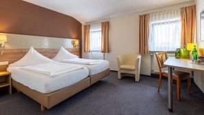 Ein Hotelzimmer mit einem Bett, zwei Nachttischen, einem Sessel, einem Schreibtisch und einer Lampe.